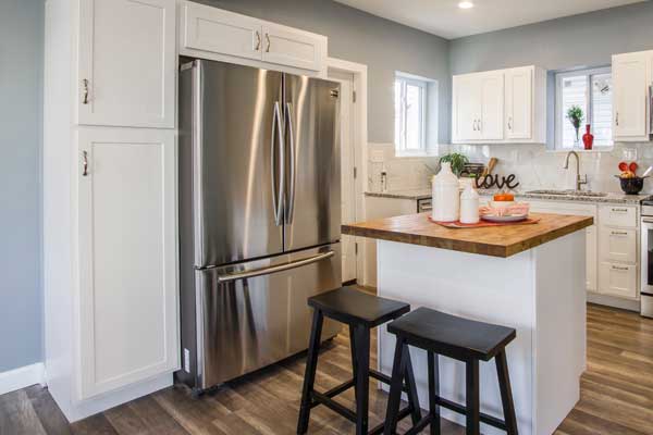 modern kitchen with white cabinetry stainless steel fridge hardwood floors and island with stools