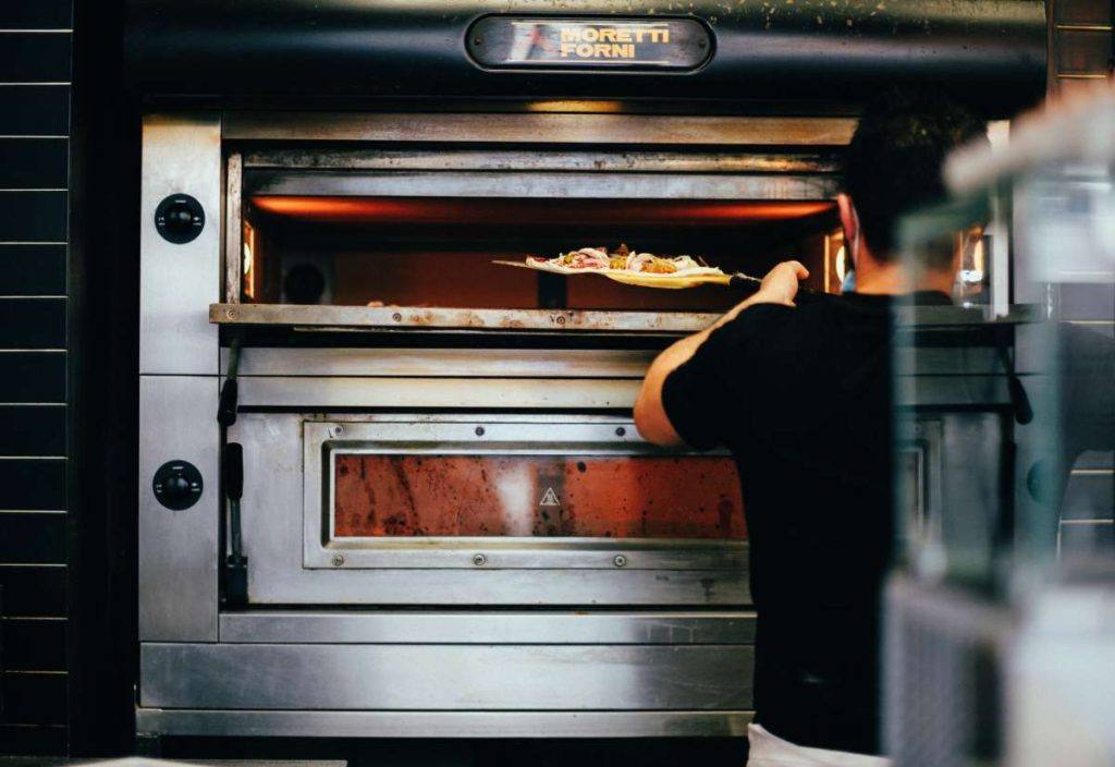 a man putting a pizza into a commercial pizza oven